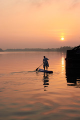 Silhouette of fat middle-aged woman on Stand Up Paddle Board at sunset in Danube river. SUP.