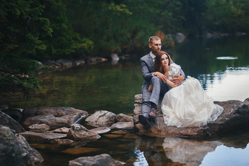 The bride and groom are sitting on a large stone in the lake. Wedding concept. Copy space