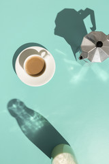 Overhead view of coffee with milk and coffee maker on pastel mint abstract background with copy space and hard shadow