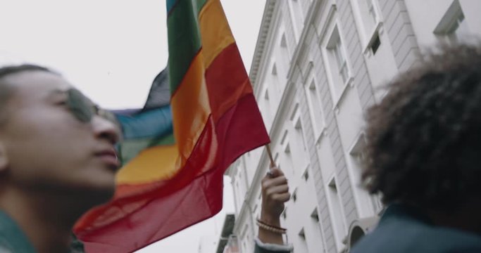 Woman waving a rainbow coloured flag at a street parade.  People attending a gay pride march in the city.
