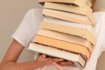 Teenage girl hiding behind the big pile of books. Student life and back to school concept