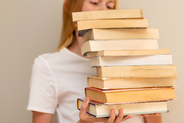 Teenage girl hiding behind the big pile of books. Student life and back to school concept