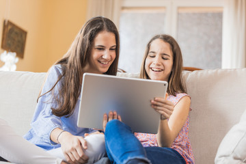 Two girls laughing looking at the tablet at home