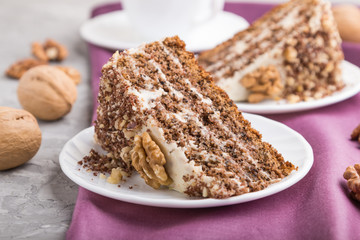 Homemade cake with milk cream and walnuts with cup of coffee on a gray concrete background, side view, selective focus.