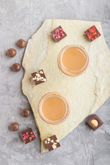 Sweet chocolate liqueur in glass on a gray concrete background and stone slate board. Top view.