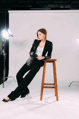 Elegant model holding digital camera near chair in photo studio