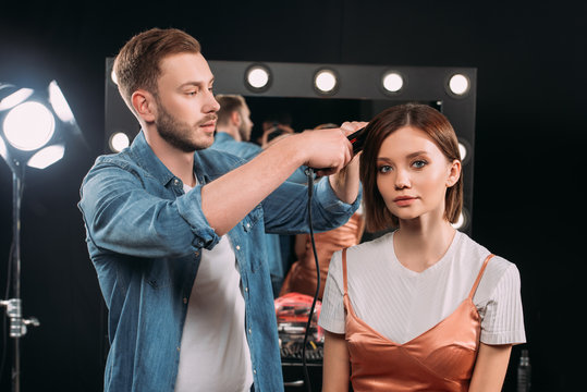 Handsome makeup artist using curling iron on hair of beautiful model in photo studio