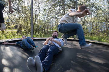 happy dad and his sons are jumping on a trampoline. children jump over dad, rejoice, have fun, laugh.