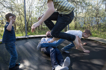 happy dad and his sons are jumping on a trampoline. children jump over dad, rejoice, have fun, laugh.