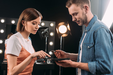 Side view of beautiful model pointing on makeup set near handsome makeup artist with cosmetic brush