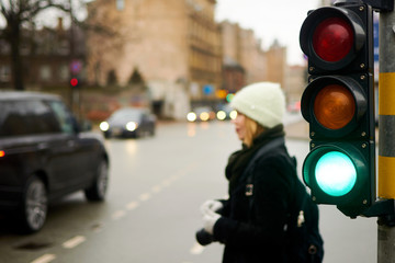 Green traffic light on a city street. A woman is waiting at a pedestrian crossing.