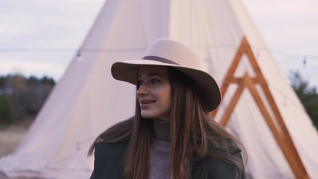 Portrait Smiling Woman in hat Stands in glamping on the background of a teepee. Concept Traveler Enjoys the Beauty of Nature. Closeup