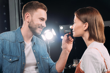 Handsome makeup artist smiling while applying lipstick on attractive model
