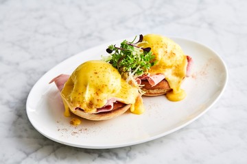 Eggs Benedict on a white plate, side view. Side view on eggs Benedict with arugula, bacon and...