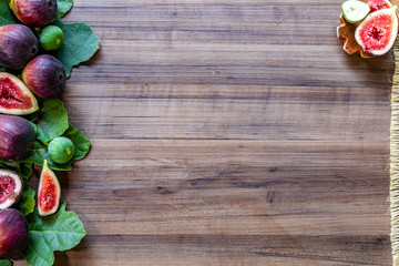 Top view of figs, green leaves on rustic wooden background