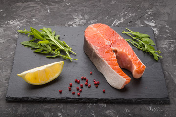 Salmon steak with arugula and lemon on a black slate board on a black concrete background. Side view.