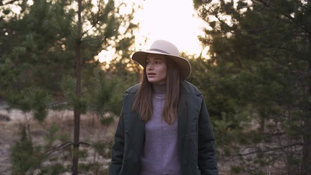 Young beautiful Woman in a hat and a warm jacket Walking In Forest At Sunset. Healthy Happy Lifestyle. Girl Hiking In The Woods. Outdoor Activities Travel Concept Man in Nature.