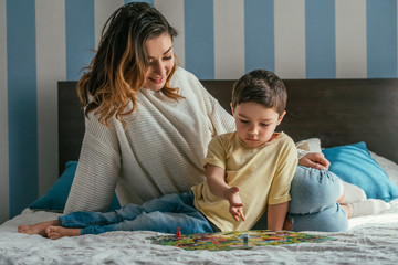 smiling mother with attentive son playing board game on bed