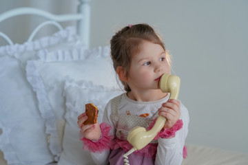 little girl talks by retro phone sitting on the bed with ruffled pillows