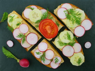 A healthy sandwiches with fresh spring vegetables. Tomato, cucumbers and radish on a black background. Vegetarian food. Top view,  flat lay.