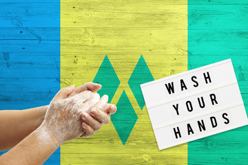 Saint Vincent And The Grenadines flag background on wooden surface. Minimal wash your hands board...