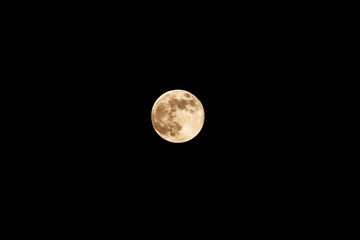 A full moon in yellow colours in the black night sky. Space and galaxy features. Bright space object. Super moon effect.