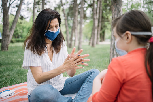 Worried mother rubbing her hands with sanitizer while sitting in park. Woman and daughter spreading hand sanitizer on their hands while enjoying fresh air in park during coronavirus pandemic.