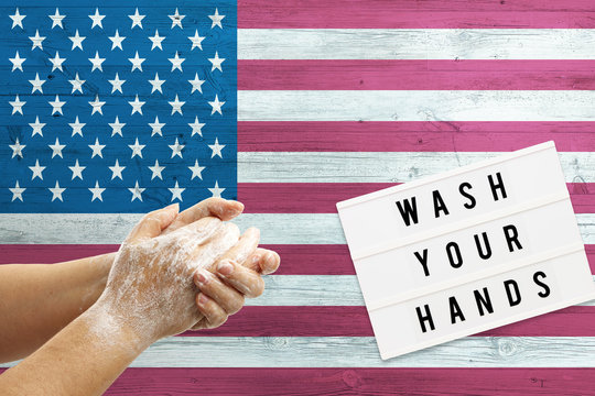 United States flag background on wooden surface. Minimal wash your hands board with minimal international hygiene concept hand detail.