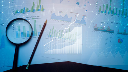 Magnifying glass and documents with analytics data lying on table