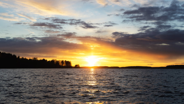 Midnight sun with water reflection at beautiful lake in finland, scandinavia, europe. Dramatic sunset over lake, waves and passing clouds. Holidays and tarvel destination.