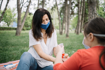 Family sitting in park and protecting themselves from virus while using hand sanitizer. Woman and child sitting in nature while using cleanser.