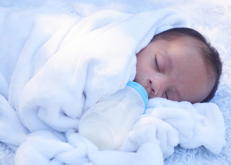 A portrait of baby eating from bottle. Little infant baby sleep on white blanket. 