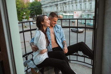 Sitting on the balcony, laughting. Quarantine lockdown, stay home concept - young beautiful caucasian couple enjoying new lifestyle during coronavirus. Happiness, togetherness, healthcare.