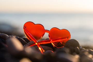 Fototapeta premium Red-heart-shaped sunglasses lie on the beach at sunset. concept of summer holidays and travel, space for text