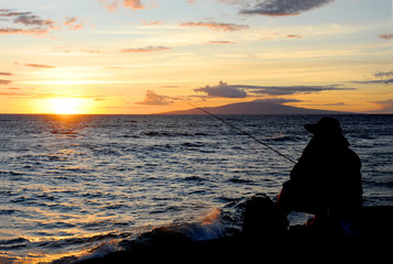 Fisherman sit on the shoreline fishing as the sun sets over the horizon on the island of Maui. 