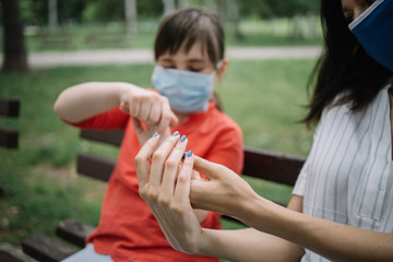 Woman and little girl sanitizing their hands with disinfectant. Cropped girls rubbing their hands with disinfectant while sitting on bench in park.