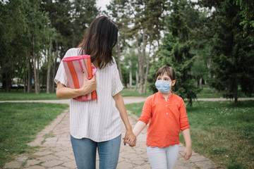 Fototapeta premium Family walking in park while wearing masks against coronavirus. Young woman and child holding their hands and wearing antivirus masks while walking in park.
