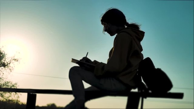 new kind of business remote online work freedom a concept with a backpack. silhouette girl working in not at home. teenage girl lifestyle with a digital tablet sits on a bench silhouette at sunset