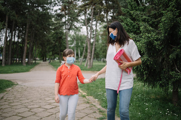Obraz premium Mother and daughter walking in park while holding their hands. Woman and child holding their hands while walking in park and wearing antivirus masks.