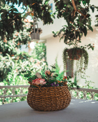 Wicker basket filled with flowers on table. Basket with artificial flowers on vernada.