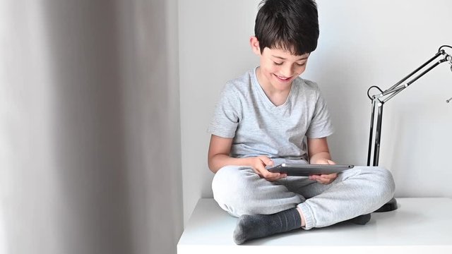 A boy playing tablet after doing homework. Home shooler. Social distance during quarantine.
