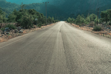 Empty rural countryside tarmac road outside Antalya. With green trees along the way and maountains in the background.