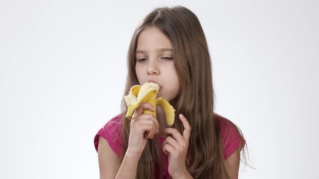 girl eating banana Little girl eating a ripe yellow banana on a white background. The girl  bites a banana and tastes it. Stock Video | Adobe Stock