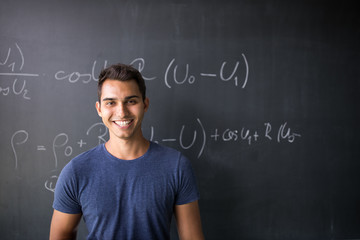 Students in a classroom - handsome student solving a math problem on a blackboard during math class - obrazy, fototapety, plakaty
