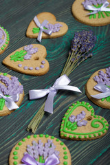 Fototapeta na wymiar Gingerbread cookies decorated with glaze. On some ribbons tied to a bow. Gingerbread cookies are round and in the shape of a heart. Near a bouquet of lavender. On brushed pine boards.
