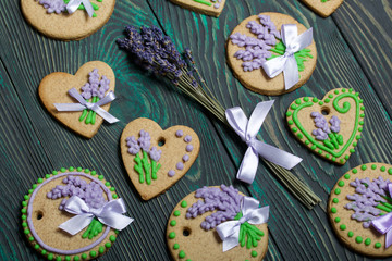 Fototapeta na wymiar Gingerbread cookies decorated with glaze. On some ribbons tied to a bow. Gingerbread cookies are round and in the shape of a heart. Near a bouquet of lavender. On brushed pine boards.