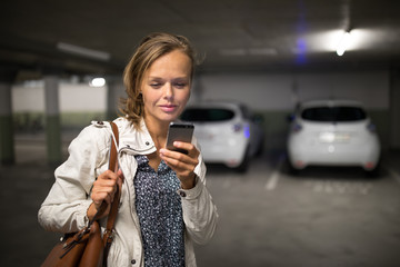 Young woman in an underground parking booking an charging an electric vehicle in an underground...
