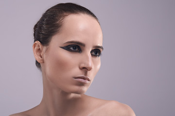 Young beautiful sexy woman with professional trendy evening glitter smoky eyes makeup, perfect shining skin, dark hair isolated on gray background studio shot