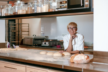 Senior female baker preparing dough for bread in modern manufacturing.