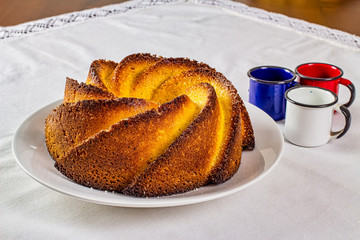 Cornmeal cake. Typical Brazilian cornmeal cake on a white porcelain plate with enameled colored agate coffee cups on the side